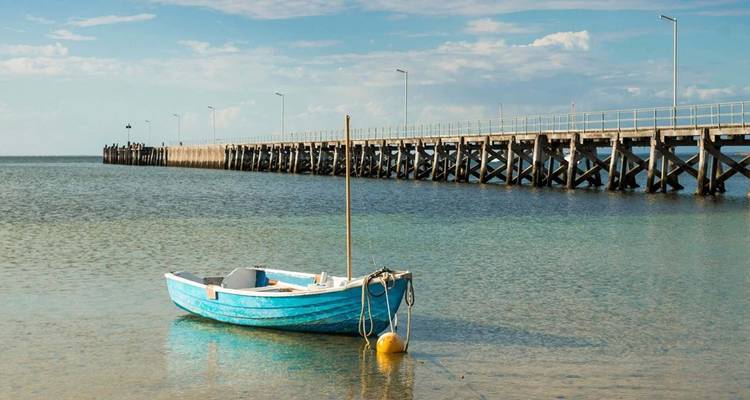 Eenzame blauwe rubberboot afgemeerd in ondiep helder water naast een lange steiger op het Eyre-schiereiland in Zuid-Australië.