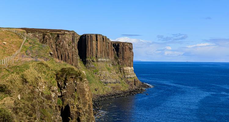 Steep sea cliffs of Kilt Rock rise above deep blue ocean on a clear day