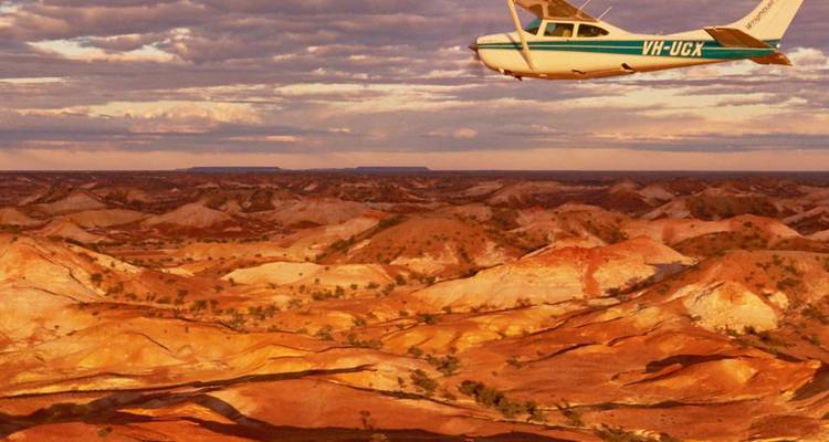 Un petit avion survole les collines striées d'ocre et de blanc du Désert Peint d'Australie au coucher du soleil.