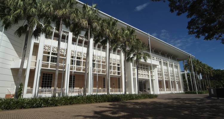 Maison du Parlement blanche moderne de Darwin encadrée par de hauts palmiers contre un ciel bleu.