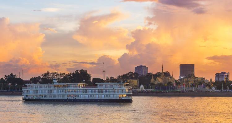 River cruise vessel passing Phnom Penh skyline bathed in dramatic orange sunset clouds.
