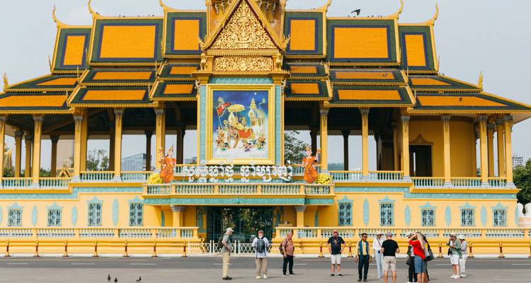 Wide view of the ornate yellow Royal Palace in Phnom Penh with visitors standing on the forecourt.