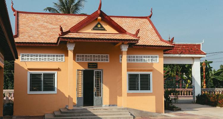 Small, tidy yellow building with red tiled roof and decorative Khmer gables set under a clear blue sky.