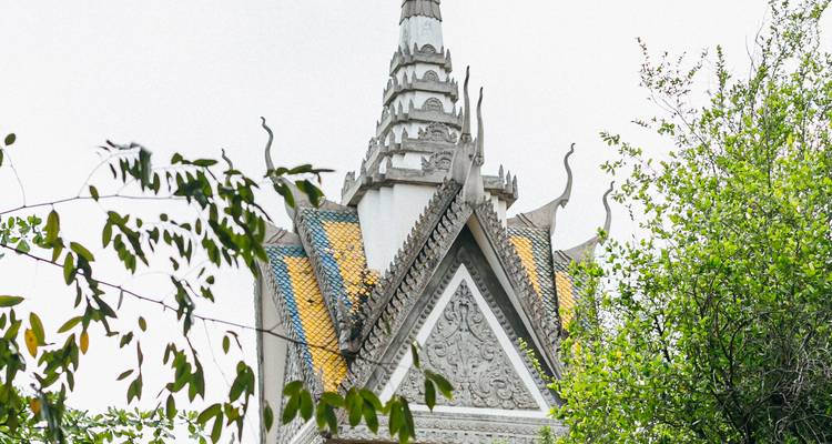 Close-up of a white stupa spire with intricate carvings and yellow tile insets, framed by leafy green branches.