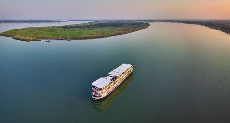 Vue aérienne d'un seul bateau de croisière glissant le long d'une large rivière verte au lever du soleil.