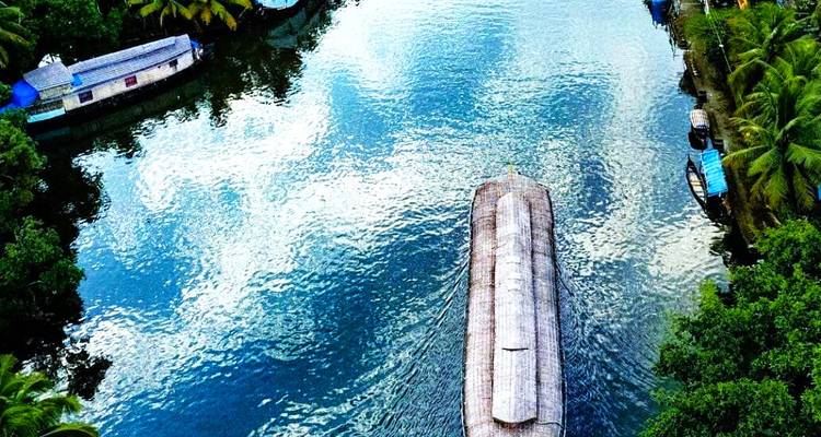 Aerial view of a traditional houseboat cruising along lush green Kerala backwaters.