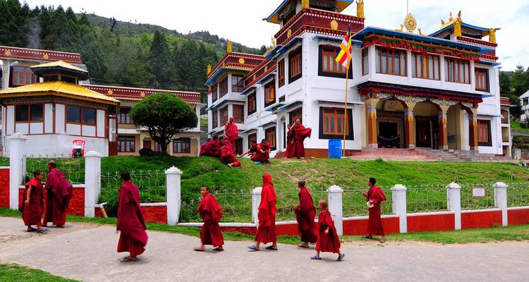 Line of red-robed monks walking past a white and red Buddhist monastery building in Tawang.