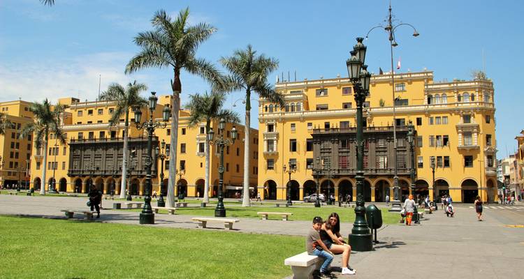 Des bâtiments coloniaux jaunes et des palmiers entourent une place spacieuse où les gens se détendent.