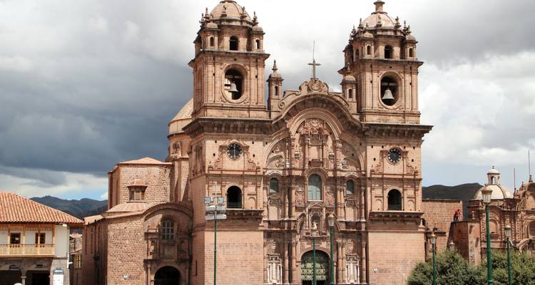 Façade baroque ornée de l'église La Compañía de Jesús sous un ciel dramatique à Cusco.