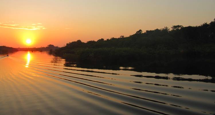 Oranje zonsondergang die reflecties werpt over een kalme rivier omzoomd door weelderig bos