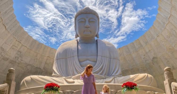 Massive seated Buddha sculpture inside a circular concrete sanctuary beneath dramatic cloud-filled sky.