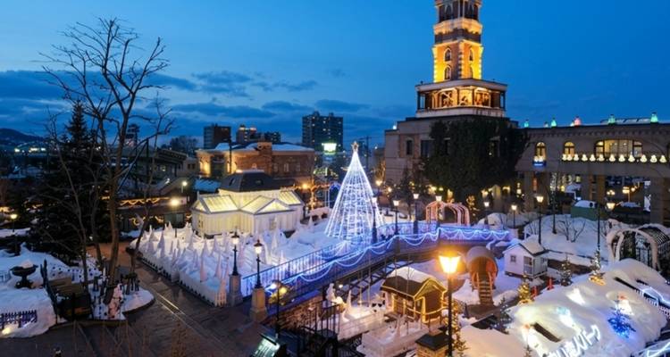 Snow-covered theme park illuminated with blue and white Christmas lights at twilight.