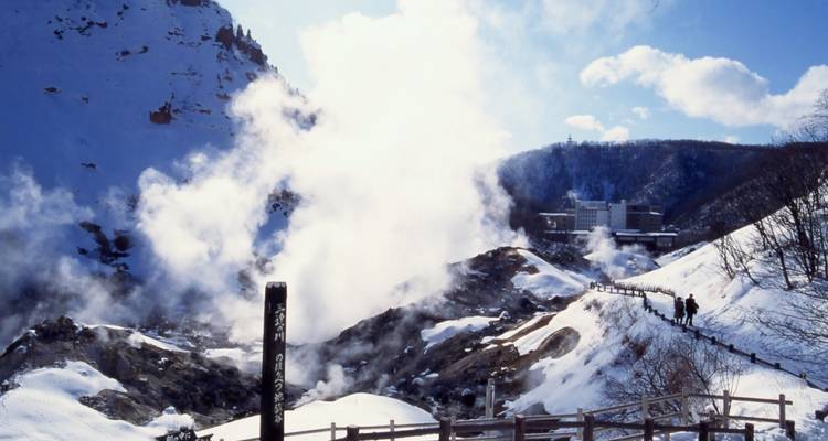 Steam billows from snow-covered volcanic valley with rugged cliffs under a bright winter sky.