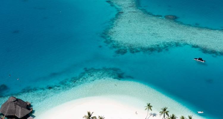Top-down view of shallow reef patterns and a lone speedboat in clear Maldives water.