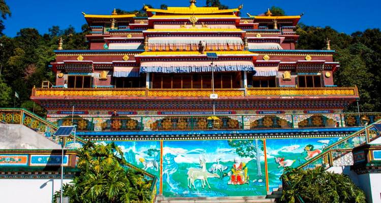Colorful multi-tiered Buddhist monastery framed by clear blue sky and forested hillside.