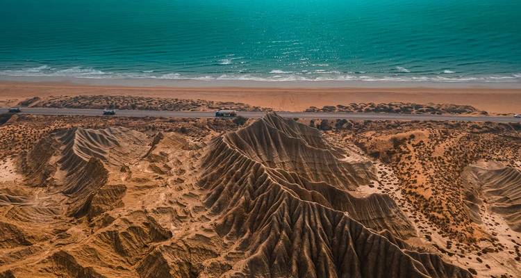 Vista aérea de espectaculares crestas de arenisca erosionadas que se encuentran con una carretera costera y un mar turquesa con una playa de arena.