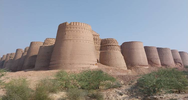 Enormes bastiones cilíndricos de una antigua fortaleza del desierto se elevan sobre vegetación escasa y terreno arenoso.
