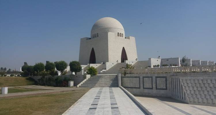 Un mausoleo de mármol blanco inmaculado con una gran cúpula se encuentra sobre una plataforma elevada contra un cielo sin nubes.