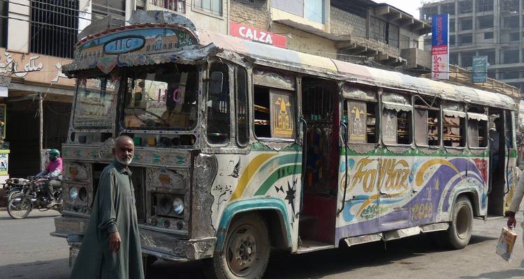 Un autobús urbano coloridamente pintado y desgastado por el tiempo, decorado con motivos, se encuentra en una bulliciosa calle urbana.
