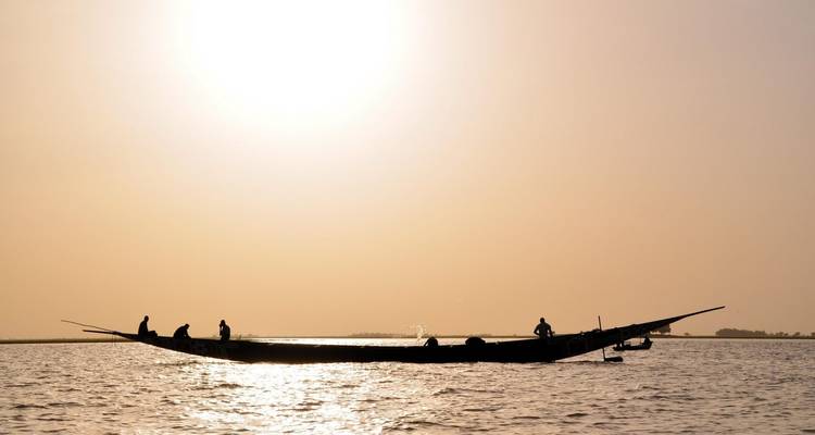 Silhouettierte Fischer auf einem schmalen Holzboot bei Sonnenuntergang auf dem Niger.
