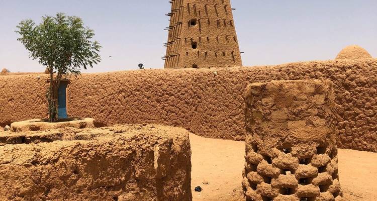 Lehmziegelwände und das ikonische Lehmziegel-Minarett von Agadez vor einem klaren Himmel.