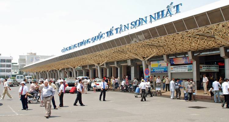 Atrio ocupado del Aeropuerto Internacional Tan Son Nhat con pasajeros, vehículos y señalización vietnamita.