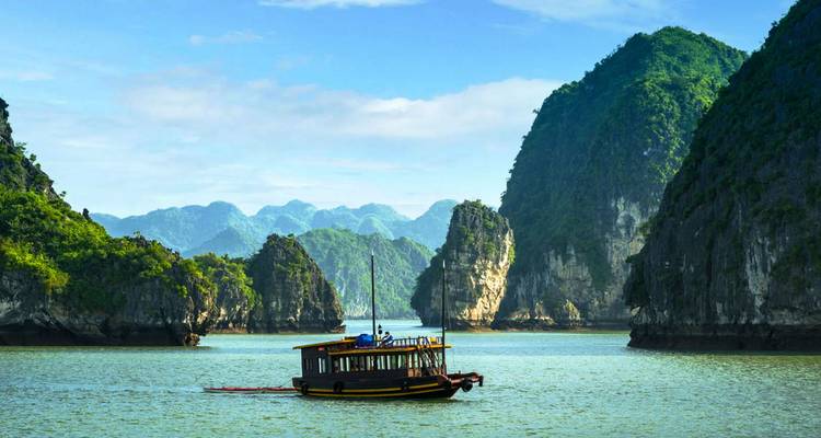 Un tradicional barco de madera navega a través de aguas esmeralda flanqueadas por espectaculares karsts de piedra caliza de la Bahía de Halong.