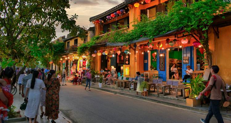 Escena nocturna de calle en Hoi An con faroles brillantes, casas comerciales amarillas y lugareños y turistas caminando junto a cafés