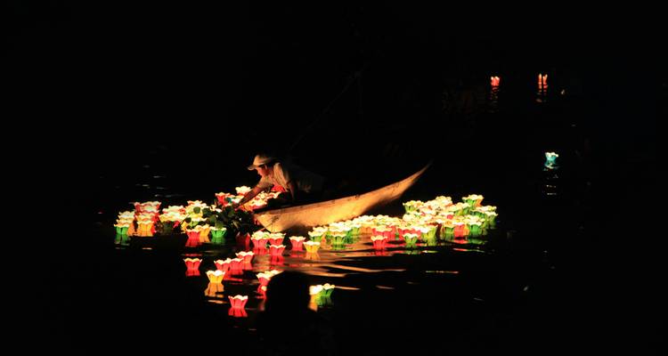 Escena nocturna de una persona en un pequeño bote liberando linternas flotantes coloridas sobre agua oscura