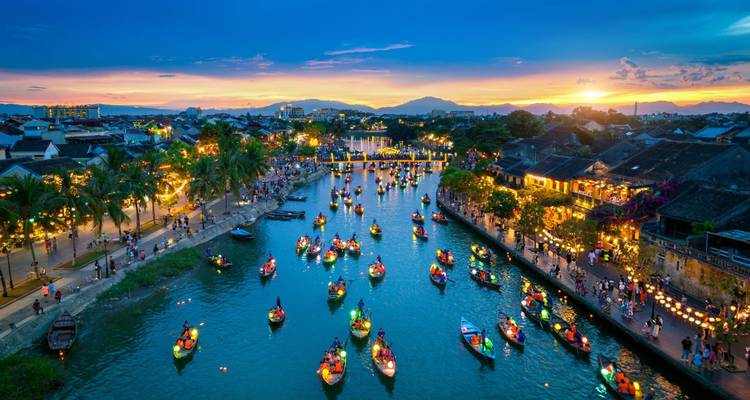 Aéreo del atardecer del río Hoi An repleto de barcos iluminados y multitudes bajo un cielo vibrante de puesta de sol