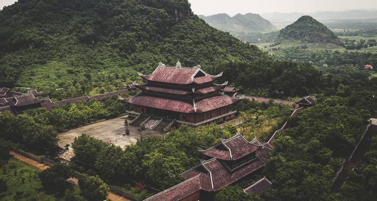 Vista de dron de un extenso complejo de templos vietnamitas con techos de pagoda ubicado entre exuberantes colinas kársticas verdes