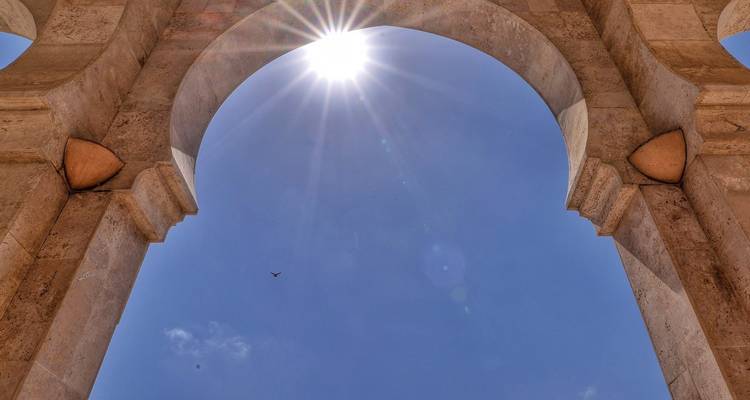 Sunlight bursts through the top of a stone archway against a clear blue sky.