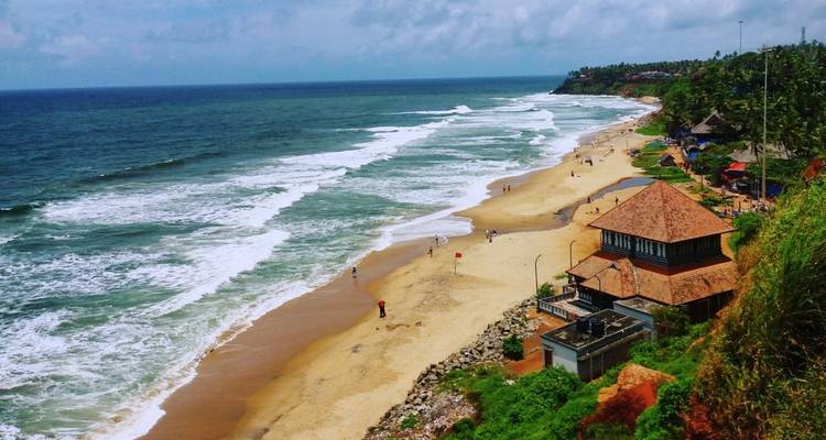 Vue spectaculaire du haut d'une falaise sur une longue plage de sable et les vagues déferlantes de l'océan bordées d'une végétation tropicale luxuriante et de cottages en bord de mer.