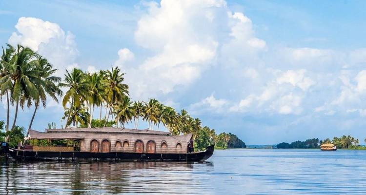 Péniche traditionnelle au toit de chaume flottant sur un lagon paisible bordé de palmiers sous un ciel bleu.