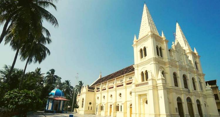 Basilique néo-gothique de couleur crème avec des flèches jumelles se dressant sous un ciel bleu clair et des palmiers qui se balancent.
