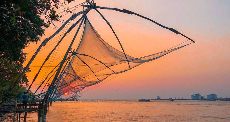 Filets de pêche chinois en silhouette contre un ciel coloré de coucher de soleil alors que le soleil plonge vers l'horizon au-dessus de l'eau.