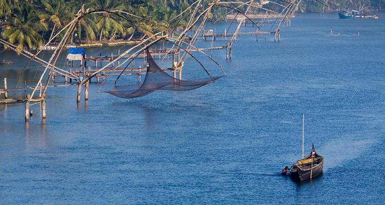 Filets de pêche chinois et un canoéiste solitaire sur un large canal de backwater bleu bordé de cocotiers.