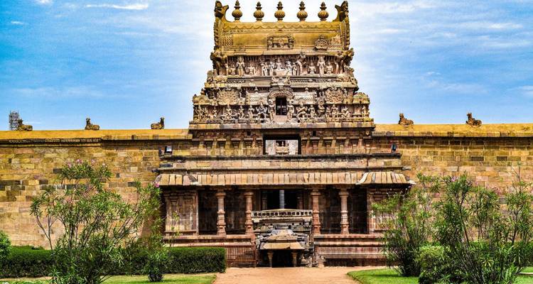 Vue de face d'une tour de temple en pierre de style dravidien richement sculptée contre un ciel bleu éclatant, avec des arbustes taillés de chaque côté.