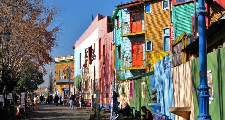 Rue pavée animée de La Boca bordée de bâtiments multicolores, d'art de rue et de visiteurs se promenant.