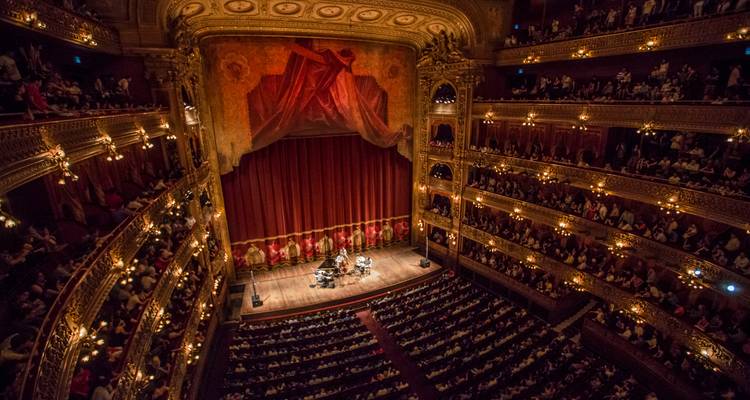 Intérieur somptueux d'un opéra bondé de spectateurs sur plusieurs balcons regardant une représentation sur la scène en contrebas.