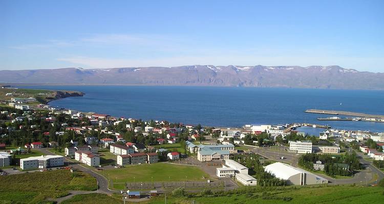 Small Icelandic town with colourful houses beside a harbour and vast fjord with mountains beyond.