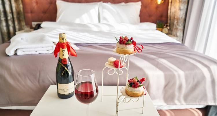 Champagne, macarons and berries are elegantly arranged on a table at the foot of a plush hotel bed.