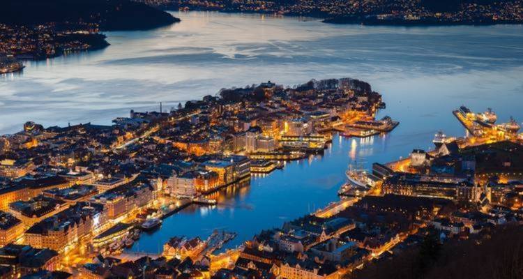 Vue aérienne crépusculaire du port illuminé de Bergen et de ses péninsules étroites entourées d'eaux sombres.
