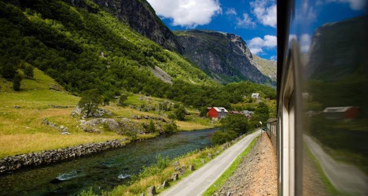 Vue depuis la fenêtre du train d'une vallée norvégienne verdoyante avec une ferme rouge au bord d'une rivière claire.