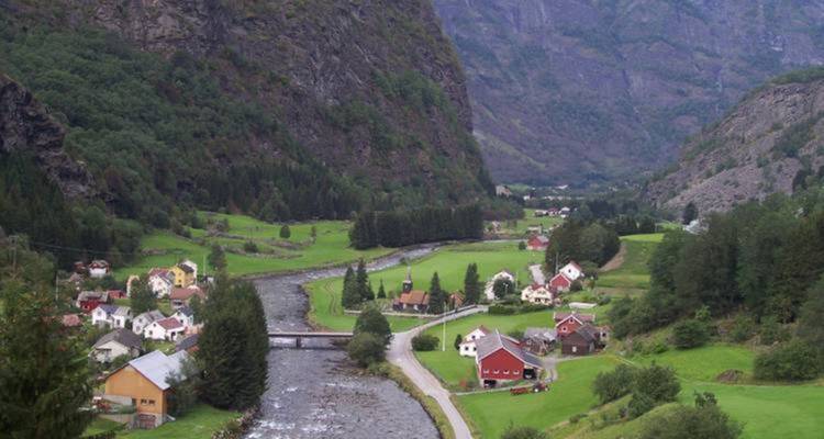Paisible village norvégien de maisons dispersées le long d'une rivière nichée entre de hautes montagnes vertes.