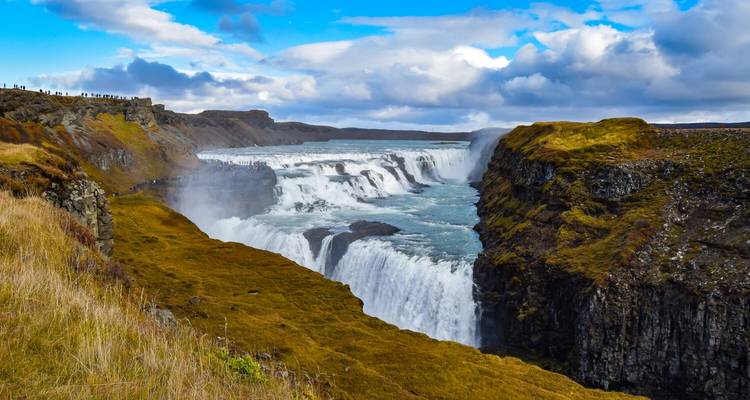 Weelderig zomerlandschap rond de Gullfoss waterval met oprijzende nevel en toeschouwers langs de bergkam.
