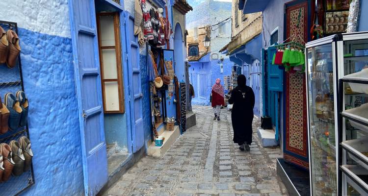 Schmale blau gestrichene Gasse von Chefchaouen mit Einheimischen, die an Kunsthandwerksläden vorbeigehen.