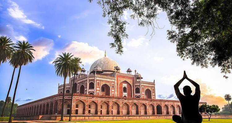 Silhouette practicing yoga in front of the ornate Humayun’s Tomb framed by palm trees and dramatic sky.