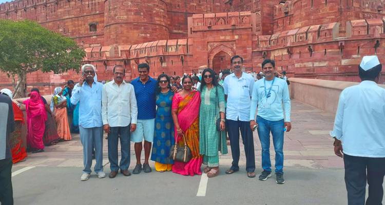 Tourist group posing in front of massive red-sandstone walls of Agra Fort on a bright day.