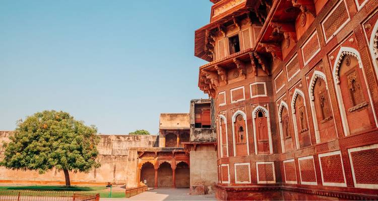 Side wing of an ornate Mughal-era red sandstone palace with arched balconies and quiet courtyard.